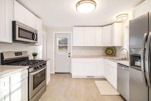 kitchen featuring stainless steel appliances, white cabinets, sink, and light hardwood / wood-style flooring