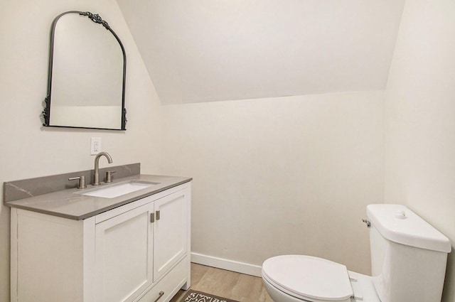 bathroom with toilet, wood-type flooring, vanity, and vaulted ceiling