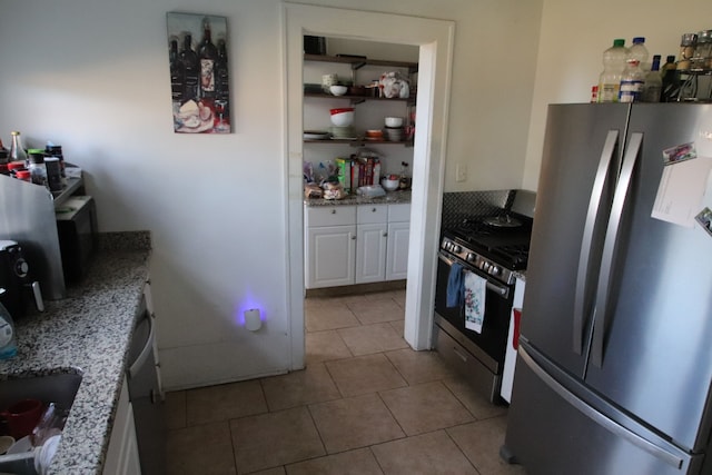 kitchen with light stone countertops, light tile patterned floors, stainless steel appliances, and white cabinetry