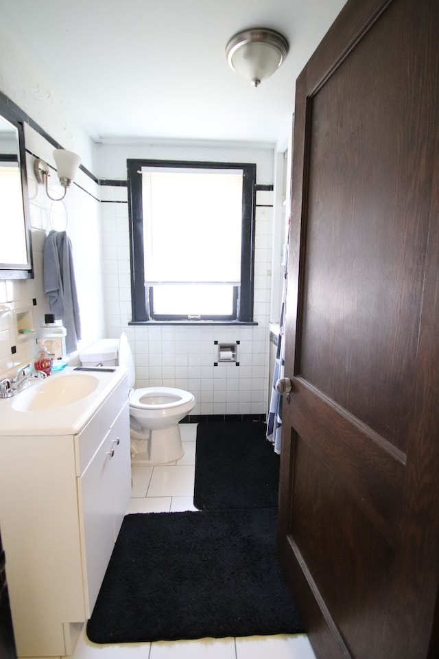 bathroom with toilet, vanity, tile patterned floors, and tile walls