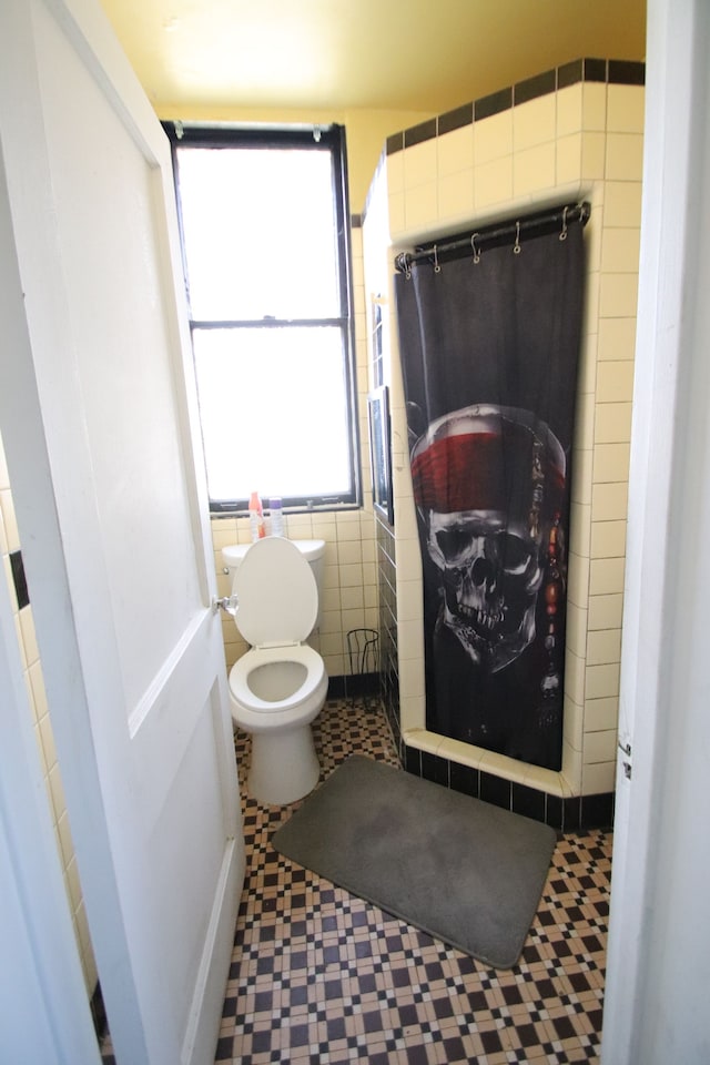 bathroom featuring tile patterned flooring, toilet, and tile walls