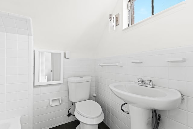 bathroom with a washtub, toilet, and tile walls