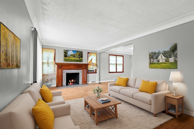 living room featuring hardwood / wood-style flooring, a premium fireplace, ornamental molding, and a textured ceiling