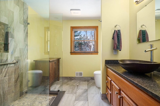 bathroom with a tile shower, vanity, and toilet