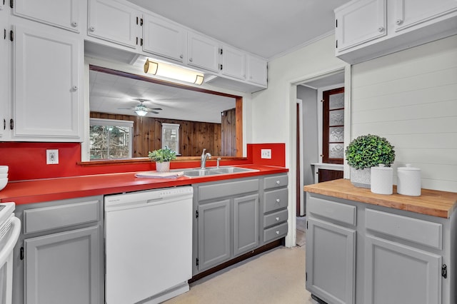 kitchen with white dishwasher, sink, wooden walls, ceiling fan, and butcher block counters