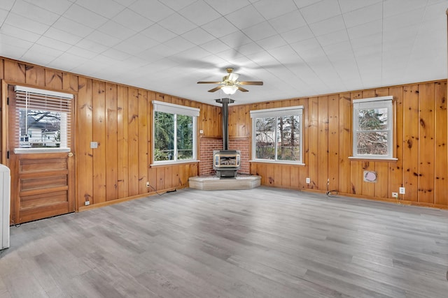 unfurnished living room with a wood stove, ceiling fan, and light hardwood / wood-style flooring