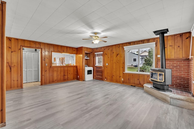 unfurnished living room with light wood-type flooring, ceiling fan, washer / dryer, a wood stove, and wood walls