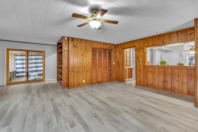 unfurnished living room featuring wooden walls, light hardwood / wood-style flooring, and ceiling fan