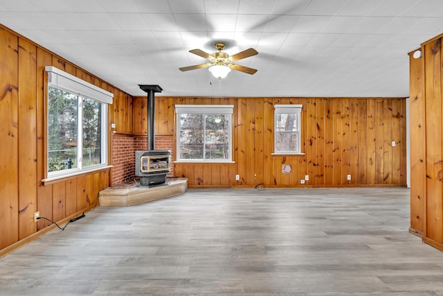 unfurnished living room with a wood stove, wooden walls, ceiling fan, and light hardwood / wood-style floors