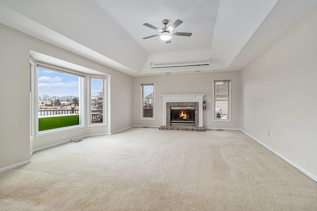 unfurnished living room with a raised ceiling, ceiling fan, carpet floors, and a brick fireplace