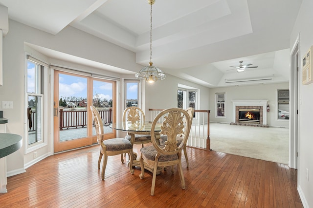 dining area with hardwood / wood-style flooring, a raised ceiling, and a brick fireplace