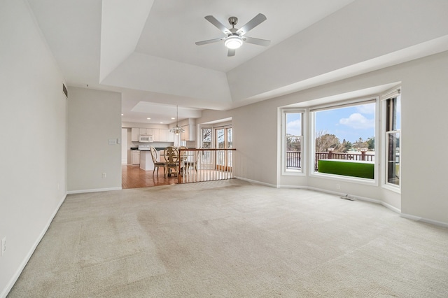 unfurnished living room featuring carpet, ceiling fan with notable chandelier, and a tray ceiling