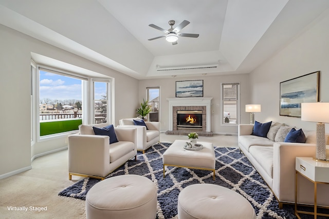 living room with carpet flooring, ceiling fan, a raised ceiling, and a fireplace