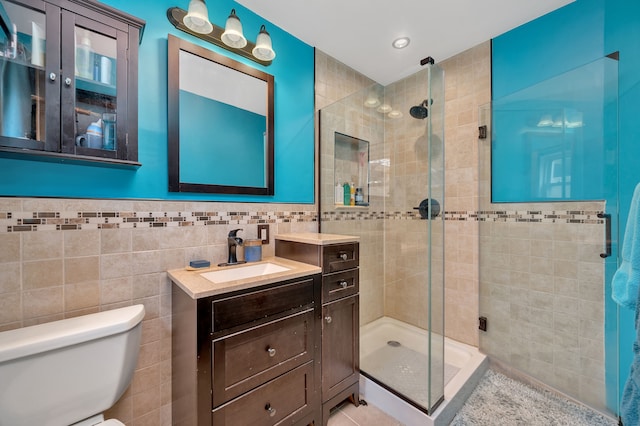 bathroom featuring a shower with door, vanity, tile walls, and toilet