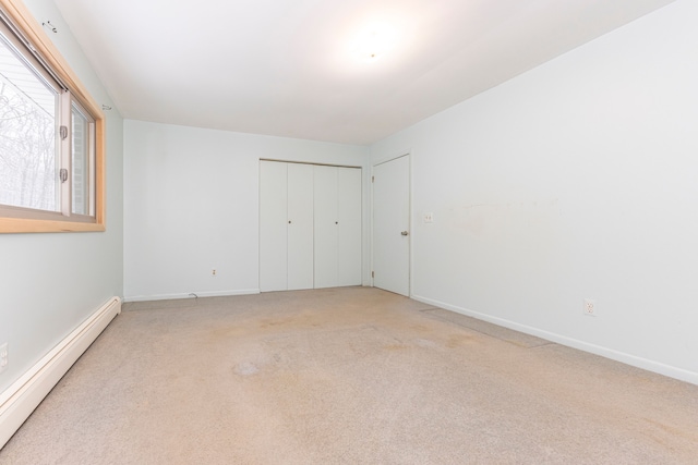 unfurnished bedroom featuring carpet, a closet, and a baseboard heating unit