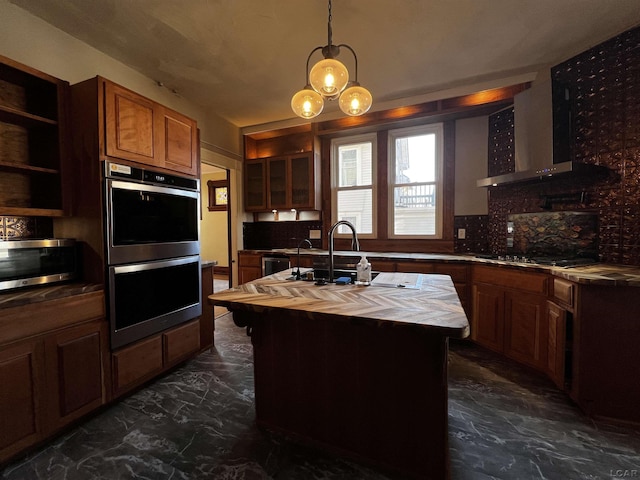 kitchen featuring stainless steel appliances, wall chimney range hood, tasteful backsplash, an island with sink, and pendant lighting