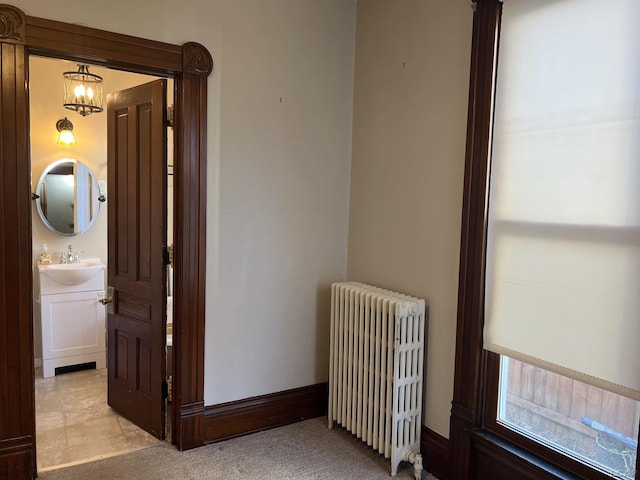 corridor with radiator heating unit, light colored carpet, a notable chandelier, and sink