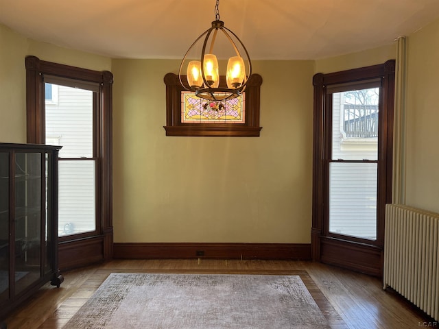 unfurnished dining area featuring radiator, light wood-type flooring, and an inviting chandelier