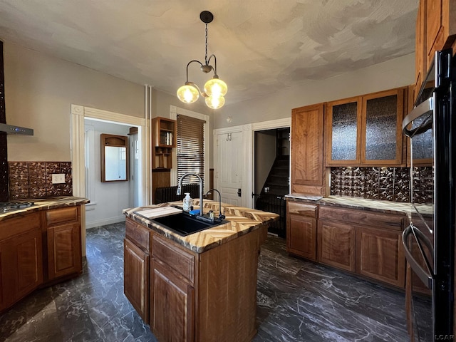 kitchen featuring sink, an inviting chandelier, backsplash, an island with sink, and decorative light fixtures