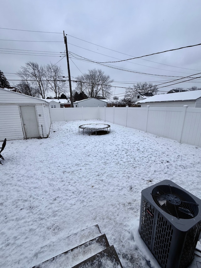 yard layered in snow with a shed, a trampoline, and central air condition unit