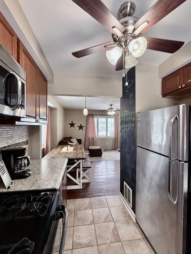 kitchen with light stone countertops, appliances with stainless steel finishes, tasteful backsplash, ceiling fan, and light tile patterned flooring