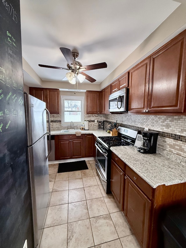 kitchen with sink, ceiling fan, light stone countertops, light tile patterned floors, and stainless steel appliances