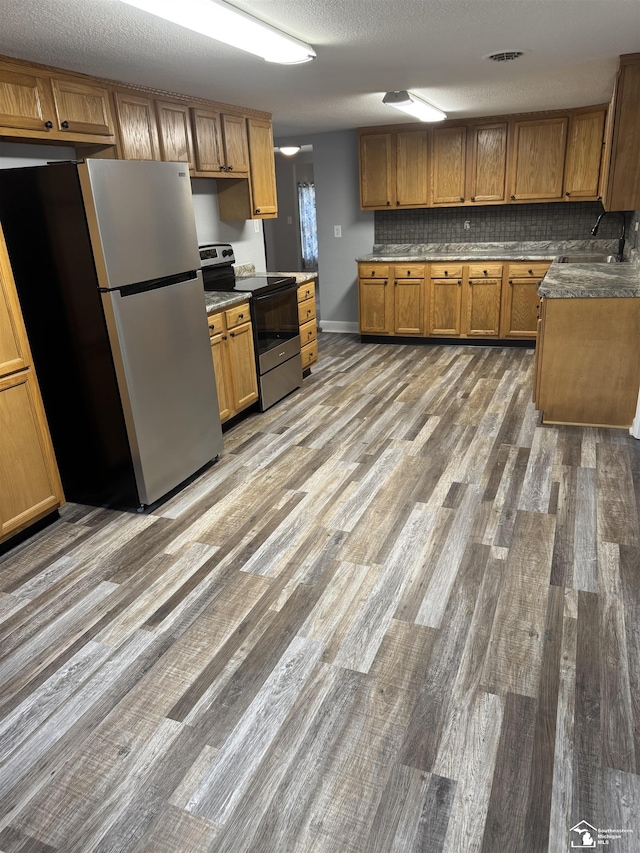 kitchen with appliances with stainless steel finishes, backsplash, a textured ceiling, sink, and hardwood / wood-style floors