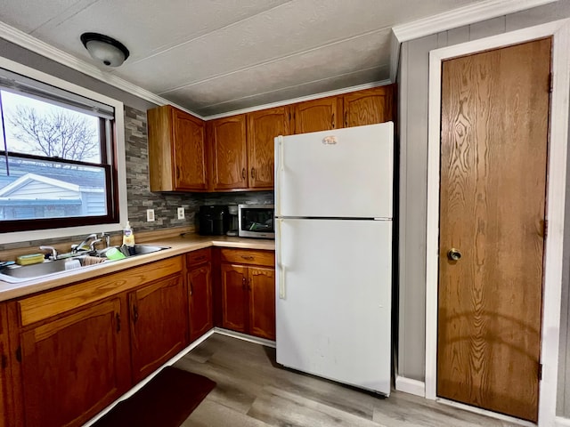 kitchen featuring sink, white refrigerator, backsplash, crown molding, and light wood-type flooring