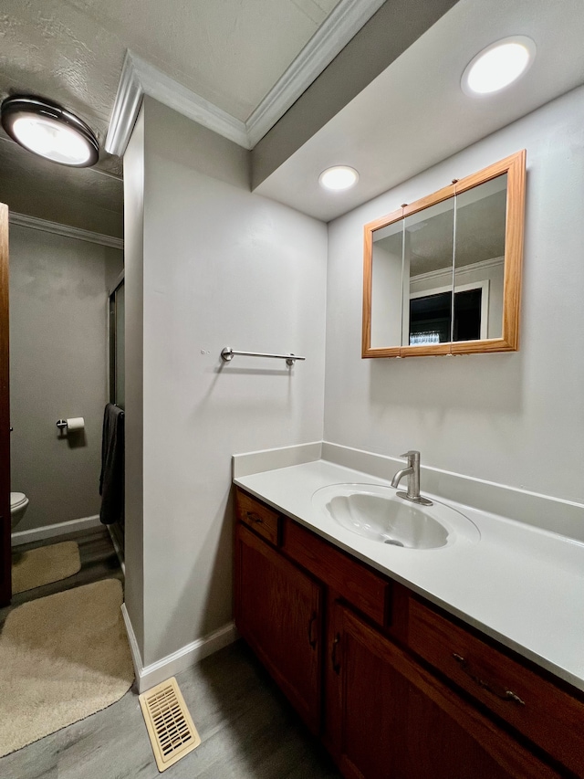 bathroom with toilet, vanity, wood-type flooring, and ornamental molding