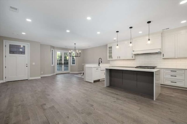 kitchen featuring dark hardwood / wood-style flooring, a kitchen island with sink, a notable chandelier, white cabinets, and hanging light fixtures