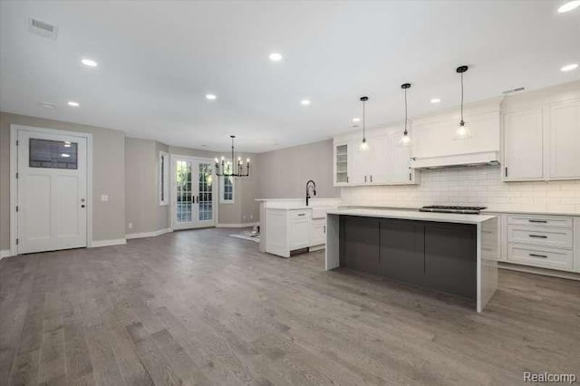 kitchen featuring dark wood-type flooring, a chandelier, pendant lighting, a kitchen island with sink, and white cabinets