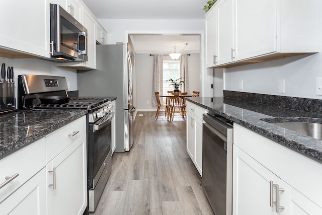 kitchen with stainless steel appliances, pendant lighting, light hardwood / wood-style flooring, dark stone countertops, and white cabinets