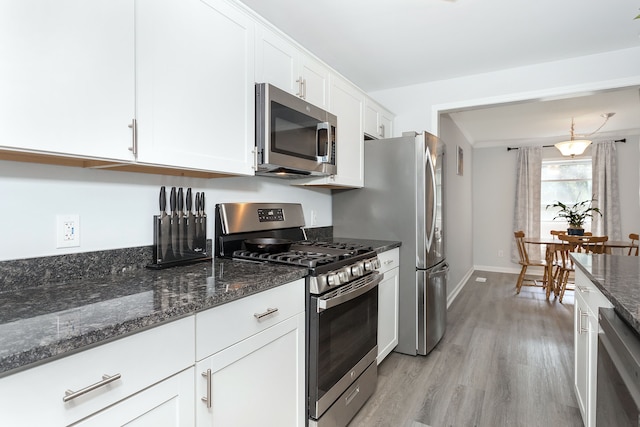 kitchen with dark stone counters, hanging light fixtures, light hardwood / wood-style floors, white cabinetry, and stainless steel appliances