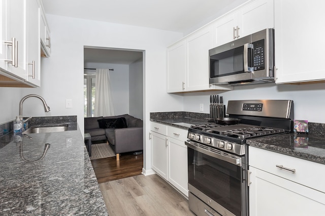 kitchen featuring white cabinetry, sink, stainless steel appliances, dark stone counters, and light hardwood / wood-style floors