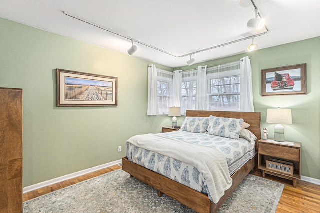 bedroom with rail lighting, baseboards, and wood finished floors