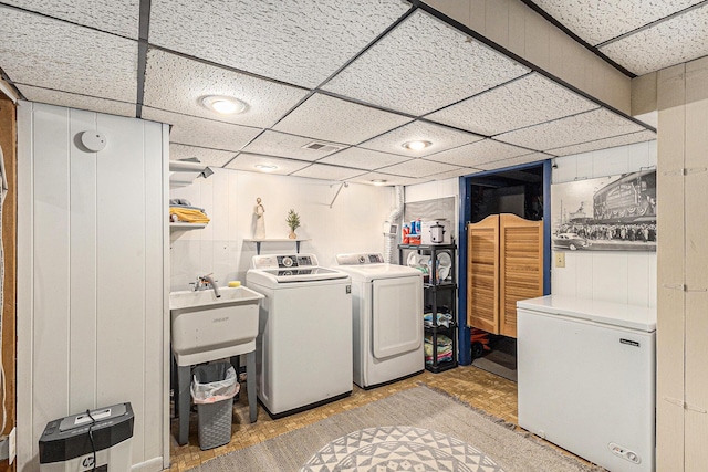 clothes washing area with washing machine and dryer, visible vents, a sink, and wood finished floors