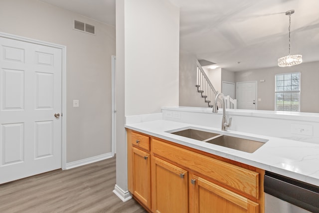 kitchen featuring dishwasher, sink, hanging light fixtures, light stone countertops, and light wood-type flooring