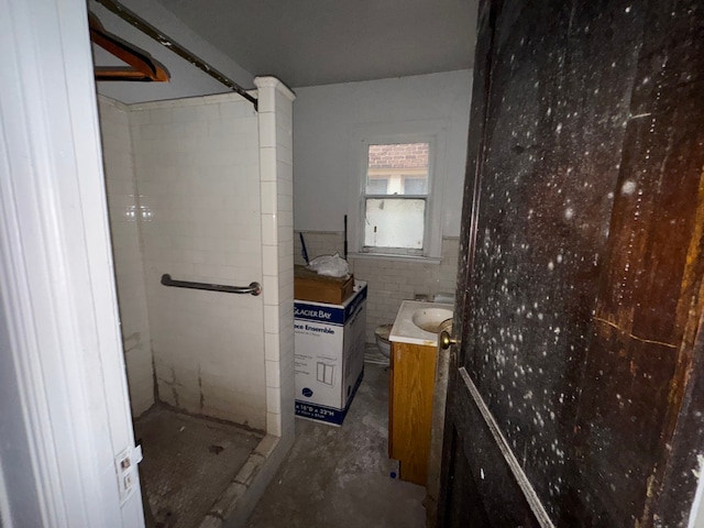 bathroom featuring a shower, vanity, concrete flooring, and tile walls