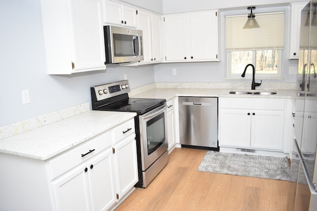 kitchen featuring appliances with stainless steel finishes, light wood-type flooring, sink, white cabinetry, and hanging light fixtures