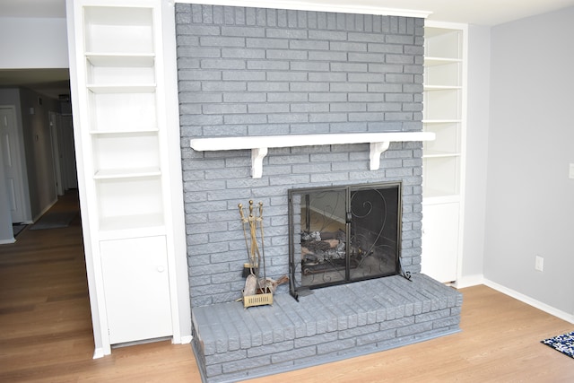 room details with hardwood / wood-style floors, built in shelves, and a brick fireplace