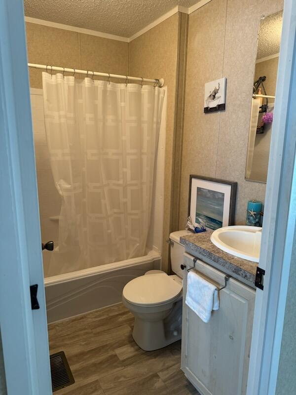 full bathroom with vanity, hardwood / wood-style flooring, toilet, shower / bathtub combination with curtain, and a textured ceiling