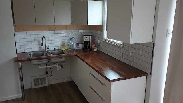 kitchen with tasteful backsplash, butcher block counters, visible vents, white cabinets, and a sink