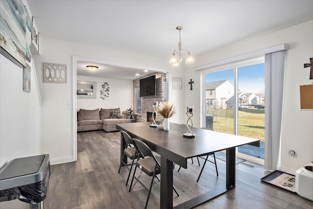 dining area featuring a stone fireplace, wood-type flooring, and a chandelier