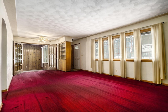 unfurnished living room featuring carpet flooring, ceiling fan, wood walls, and a textured ceiling