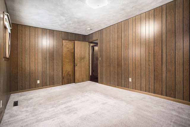 carpeted spare room with a textured ceiling and wooden walls