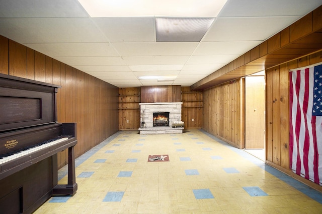 basement featuring a paneled ceiling, wood walls, and a fireplace