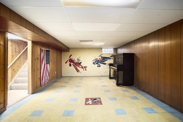 basement featuring wooden walls and a drop ceiling