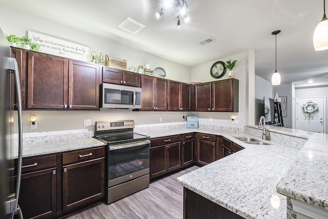 kitchen featuring sink, light stone counters, decorative light fixtures, appliances with stainless steel finishes, and light wood-type flooring