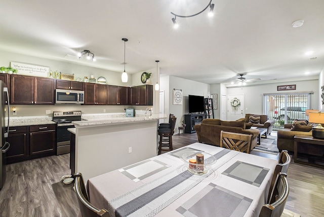 kitchen featuring appliances with stainless steel finishes, a kitchen breakfast bar, light stone counters, dark wood-type flooring, and decorative light fixtures