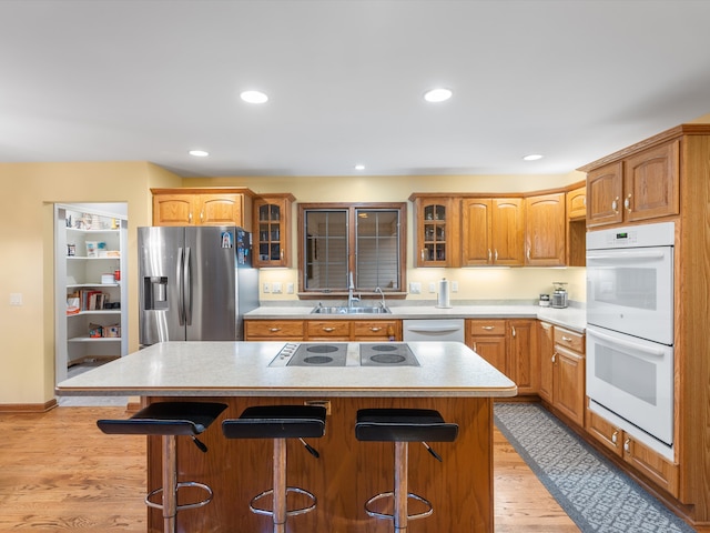 kitchen with a breakfast bar, white appliances, sink, light hardwood / wood-style floors, and a kitchen island